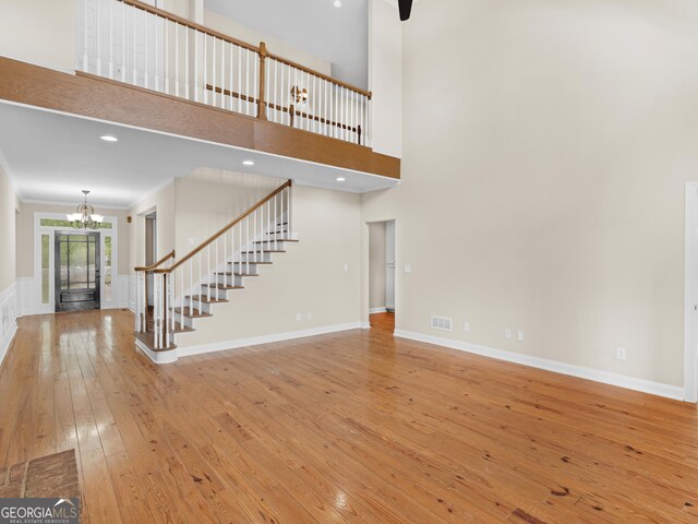 unfurnished living room featuring a towering ceiling, wood-type flooring, ornamental molding, and a notable chandelier