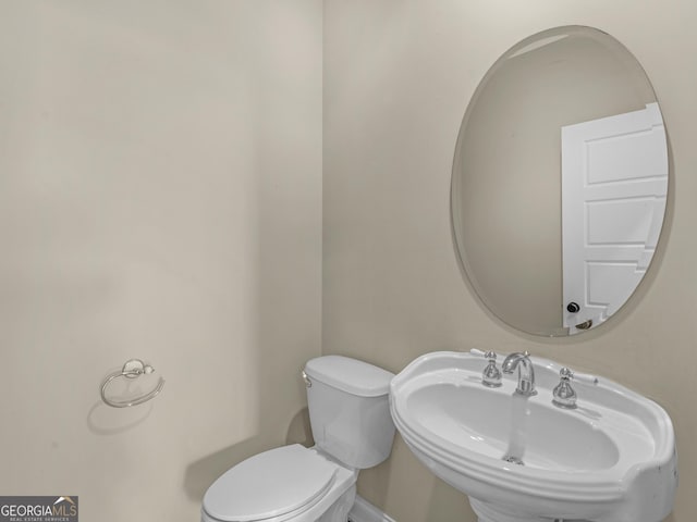 half bathroom with baseboards, a sink, and toilet