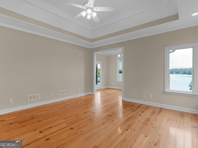 spare room with a ceiling fan, visible vents, crown molding, a tray ceiling, and light wood-style flooring
