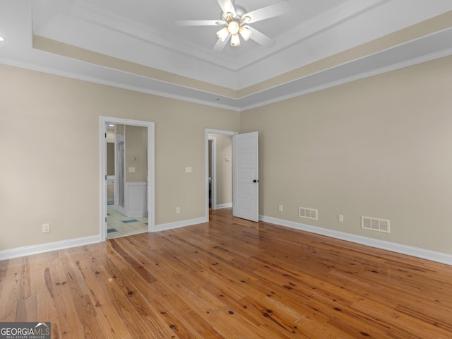 unfurnished bedroom with light wood-style floors, ornamental molding, a tray ceiling, and visible vents