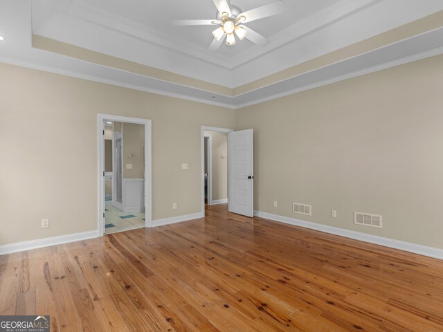 unfurnished bedroom featuring crown molding, a tray ceiling, light hardwood / wood-style flooring, and ensuite bath