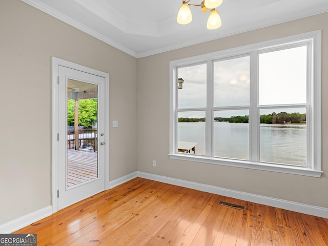 empty room featuring an inviting chandelier, a water view, ornamental molding, light hardwood / wood-style floors, and a raised ceiling