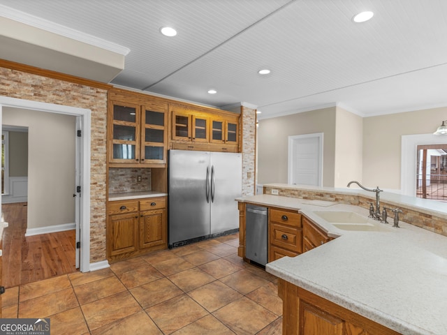 kitchen with crown molding, appliances with stainless steel finishes, brown cabinets, a sink, and light countertops
