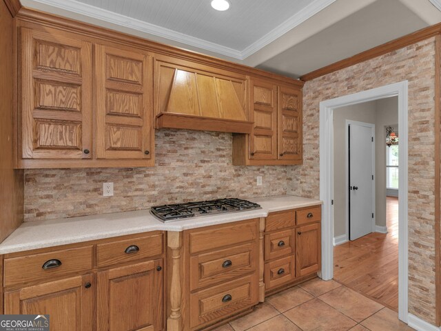 kitchen featuring range hood, ornamental molding, stainless steel gas cooktop, light tile patterned flooring, and decorative backsplash