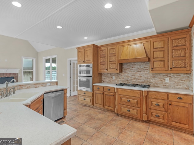 kitchen featuring appliances with stainless steel finishes, sink, backsplash, a brick fireplace, and custom range hood