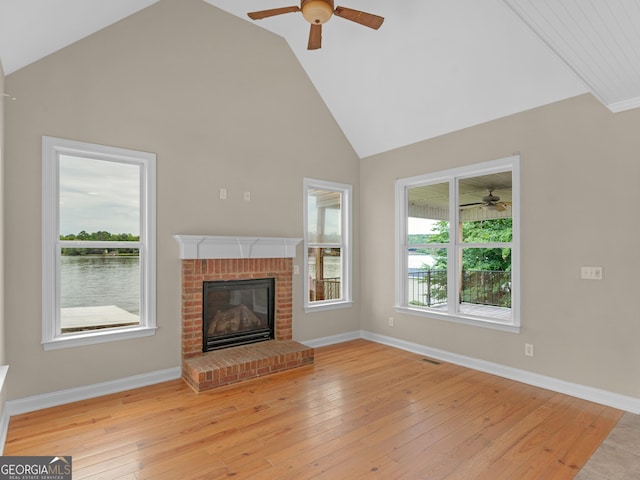 unfurnished living room featuring light wood-style flooring, a brick fireplace, ceiling fan, and high vaulted ceiling