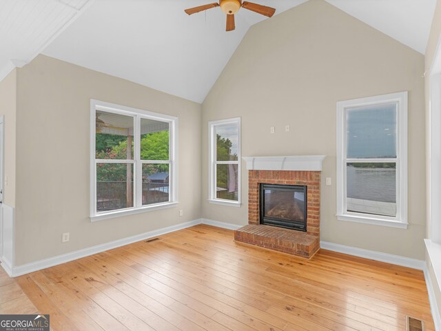 unfurnished living room with ceiling fan, high vaulted ceiling, a fireplace, and light wood-type flooring