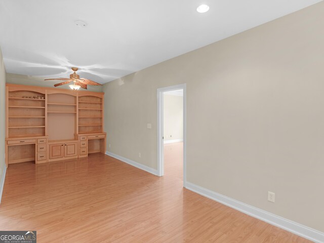 unfurnished living room featuring built in desk, ceiling fan, and light wood-type flooring