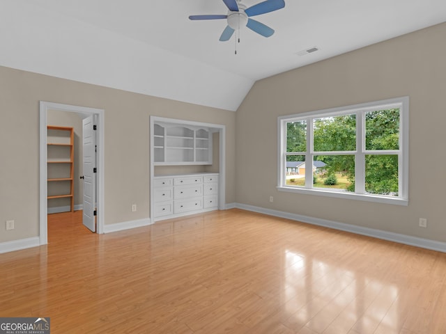 unfurnished bedroom with a walk in closet, lofted ceiling, and light hardwood / wood-style flooring