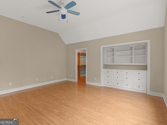 unfurnished bedroom with ceiling fan, a walk in closet, light wood-style flooring, baseboards, and lofted ceiling