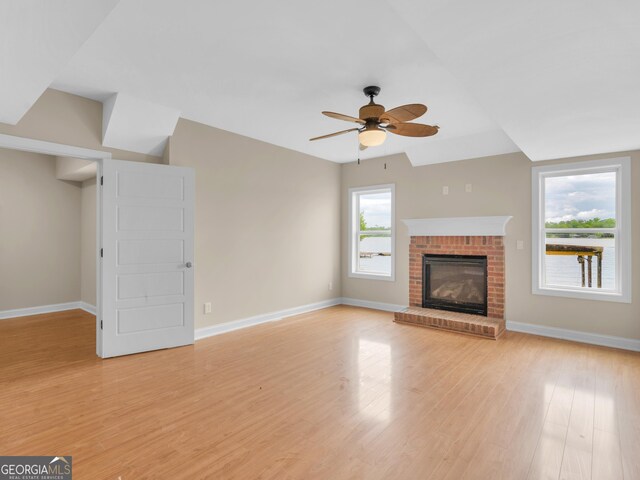 unfurnished living room with lofted ceiling, a fireplace, light hardwood / wood-style flooring, and ceiling fan