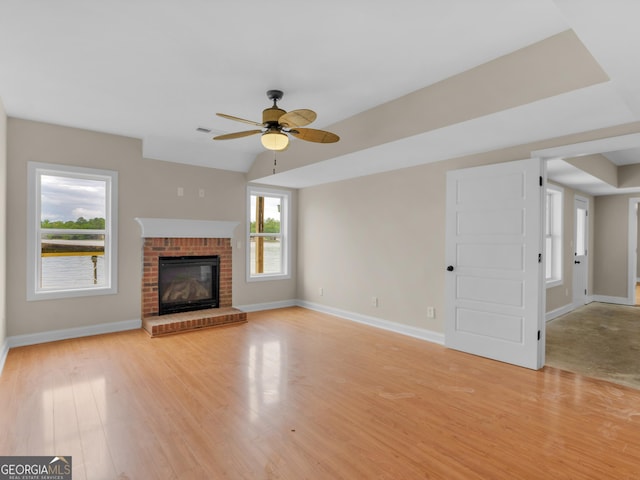 unfurnished living room featuring baseboards, ceiling fan, a brick fireplace, and light wood finished floors