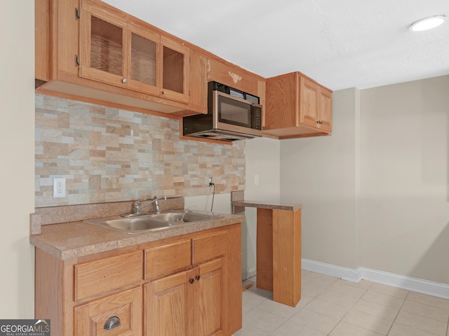 kitchen featuring decorative backsplash, light tile patterned flooring, light countertops, stainless steel microwave, and a sink