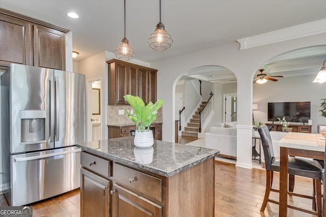 kitchen with stone counters, hanging light fixtures, stainless steel refrigerator with ice dispenser, a kitchen island, and light wood-type flooring