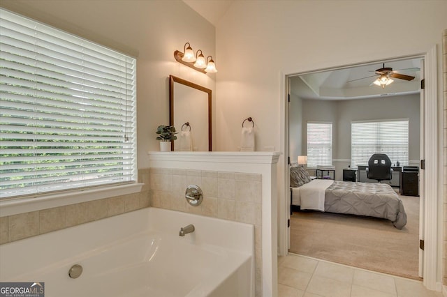 bathroom with tile patterned flooring, a raised ceiling, ceiling fan, and a tub to relax in