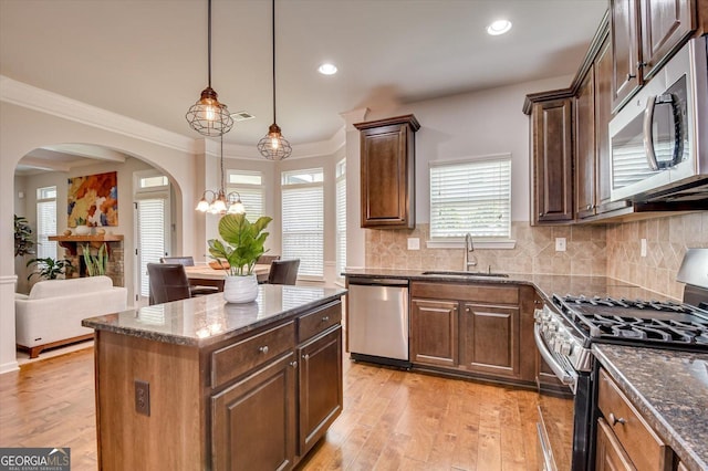 kitchen featuring sink, light hardwood / wood-style flooring, dark stone counters, pendant lighting, and stainless steel appliances