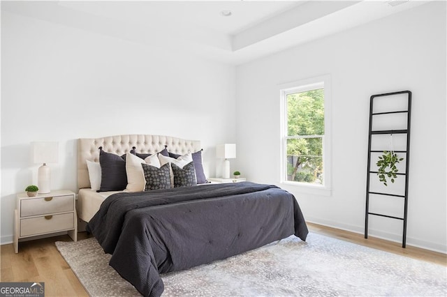 bedroom with light wood-type flooring and a tray ceiling