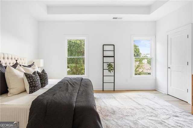 bedroom with a tray ceiling, multiple windows, visible vents, and light wood-type flooring