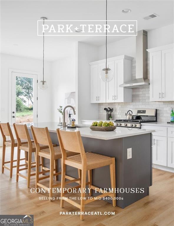 kitchen featuring a breakfast bar, wall chimney range hood, light hardwood / wood-style floors, decorative light fixtures, and gas range