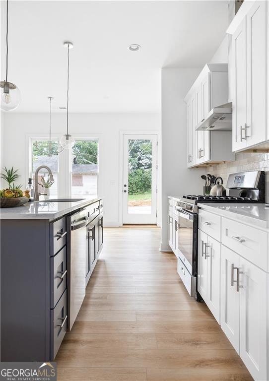 kitchen featuring white cabinetry, light hardwood / wood-style flooring, tasteful backsplash, stainless steel appliances, and pendant lighting