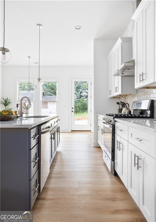 kitchen featuring light wood-type flooring, a sink, under cabinet range hood, white cabinetry, and stainless steel appliances