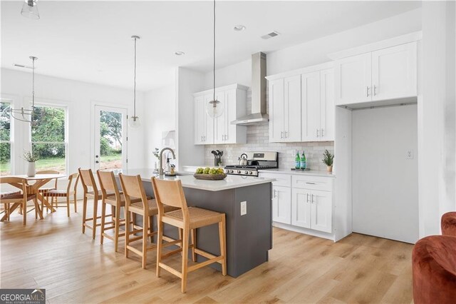 kitchen with tasteful backsplash, range, pendant lighting, light wood-type flooring, and wall chimney exhaust hood