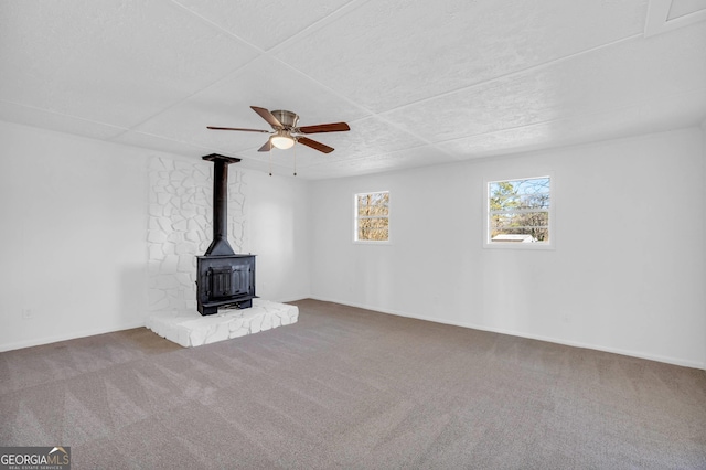 unfurnished living room with a wood stove, carpet, and ceiling fan