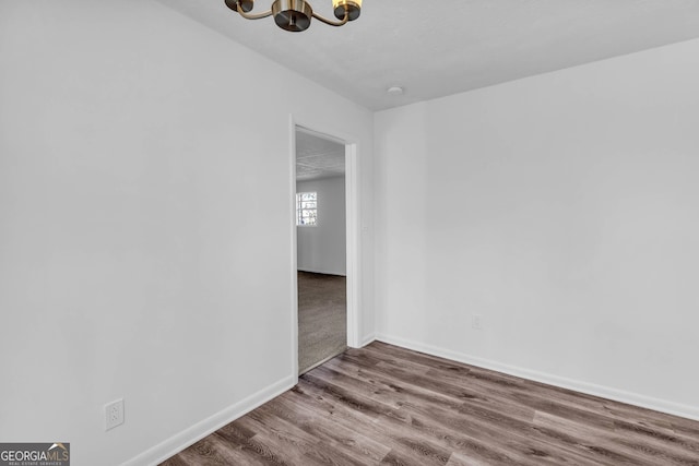 empty room with wood-type flooring and a notable chandelier