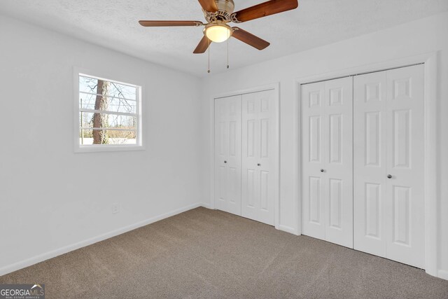 unfurnished bedroom with two closets, carpet floors, and ceiling fan