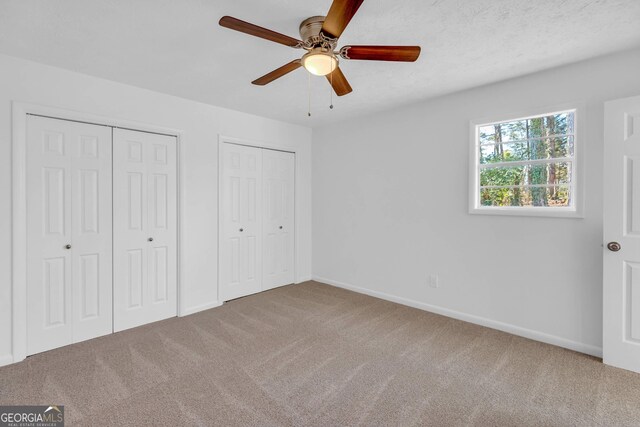 unfurnished bedroom with multiple closets, ceiling fan, and carpet flooring