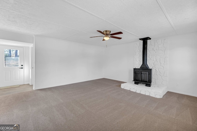 unfurnished living room with a wood stove, a textured ceiling, carpet floors, and ceiling fan