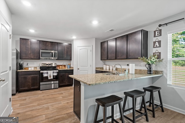 kitchen with dark brown cabinets, light wood-type flooring, sink, and appliances with stainless steel finishes