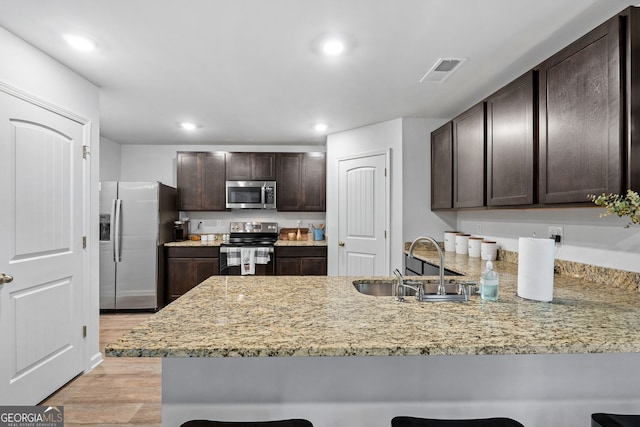 kitchen featuring kitchen peninsula, appliances with stainless steel finishes, light wood-type flooring, and dark brown cabinets