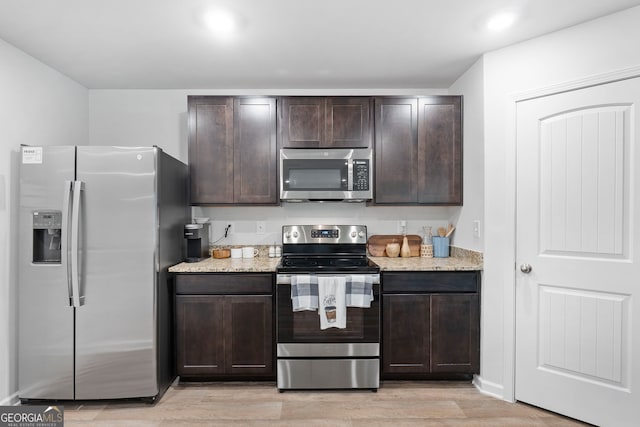 kitchen with dark brown cabinetry, stainless steel appliances, light hardwood / wood-style flooring, and light stone counters