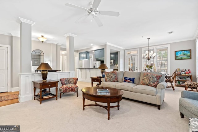 living room featuring decorative columns, ornamental molding, light carpet, and ceiling fan with notable chandelier