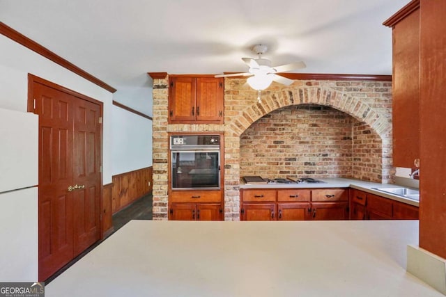 kitchen with stainless steel gas cooktop, crown molding, sink, white fridge, and black oven