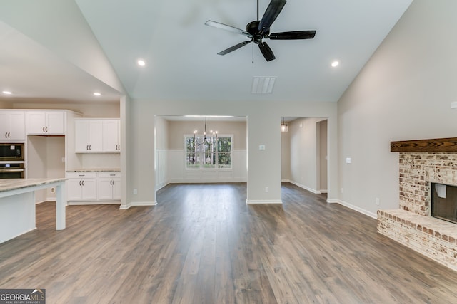 unfurnished living room with lofted ceiling, a brick fireplace, ceiling fan with notable chandelier, and hardwood / wood-style floors