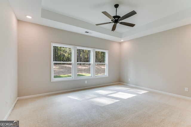 empty room with ceiling fan, light carpet, and a tray ceiling