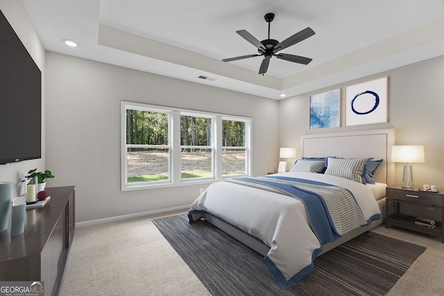 bedroom with light carpet, a tray ceiling, and ceiling fan