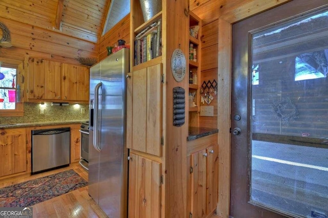 kitchen featuring stainless steel appliances, light stone counters, tasteful backsplash, lofted ceiling with beams, and wood walls