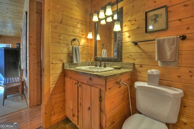 bathroom with vanity, toilet, and wood walls