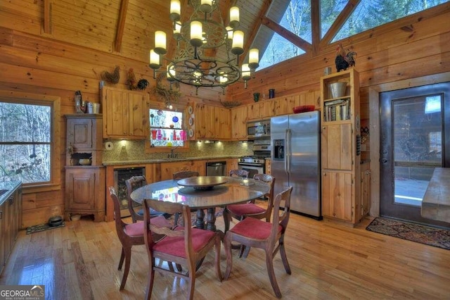 kitchen with an inviting chandelier, high vaulted ceiling, hanging light fixtures, light wood-type flooring, and stainless steel appliances