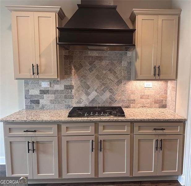 kitchen featuring light stone counters, decorative backsplash, stainless steel gas cooktop, and custom exhaust hood