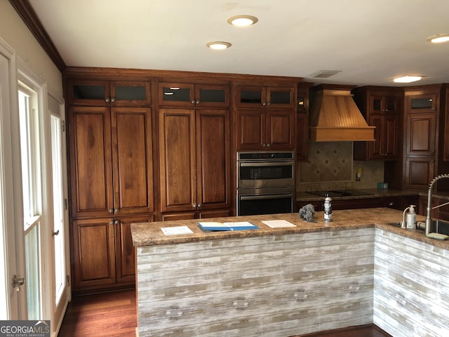 kitchen with custom exhaust hood, double oven, sink, light stone counters, and black electric cooktop