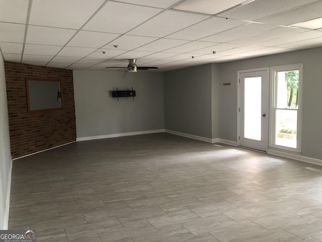 empty room with a drop ceiling, brick wall, and ceiling fan