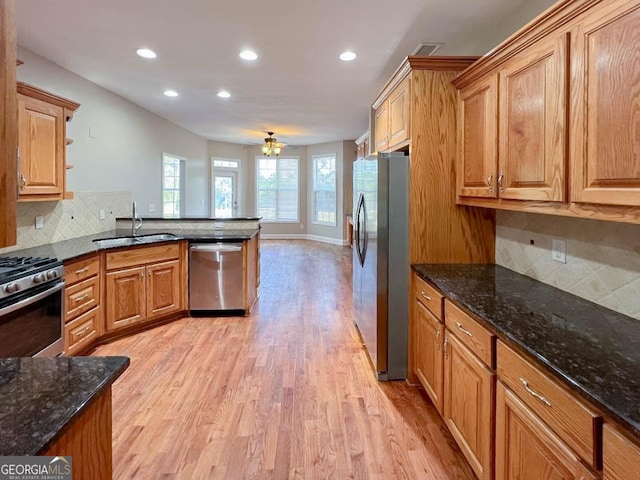 kitchen featuring sink, light hardwood / wood-style floors, dark stone counters, and appliances with stainless steel finishes