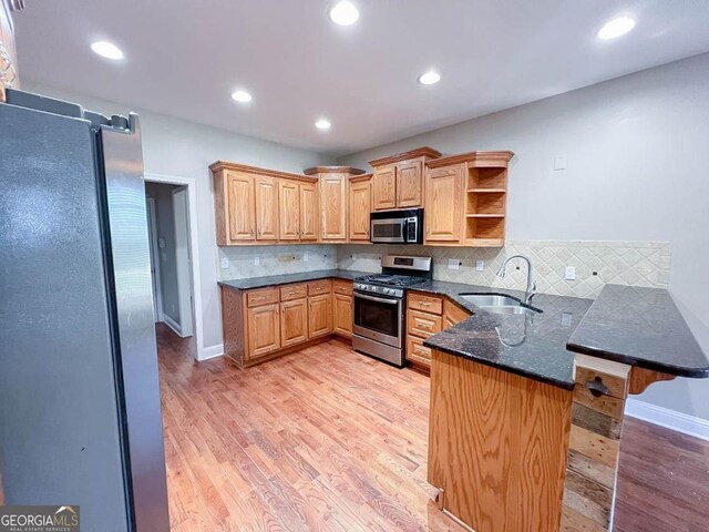 kitchen featuring sink, light wood-type flooring, kitchen peninsula, stainless steel appliances, and decorative backsplash