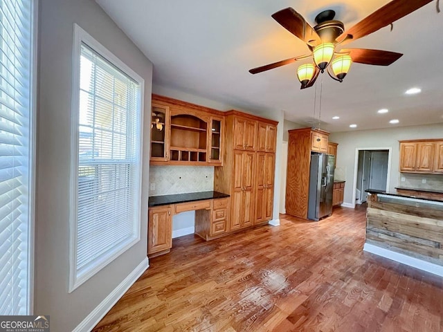 kitchen with built in desk, backsplash, hardwood / wood-style flooring, ceiling fan, and stainless steel refrigerator with ice dispenser