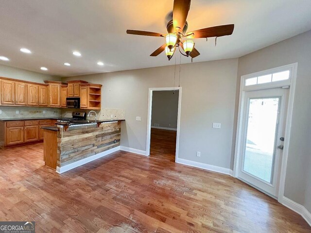 kitchen featuring stainless steel range, kitchen peninsula, decorative backsplash, and light wood-type flooring