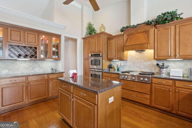 kitchen with light wood-type flooring, a high ceiling, dark stone counters, ceiling fan, and stainless steel appliances